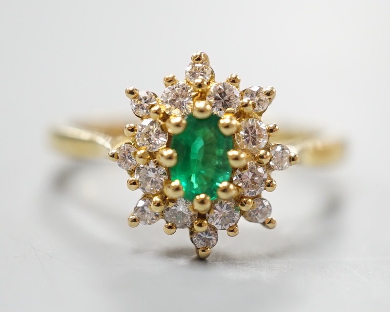 A modern 18ct gold, emerald and diamond set star shaped cluster ring, size L/M, gross weight 3.8 grams